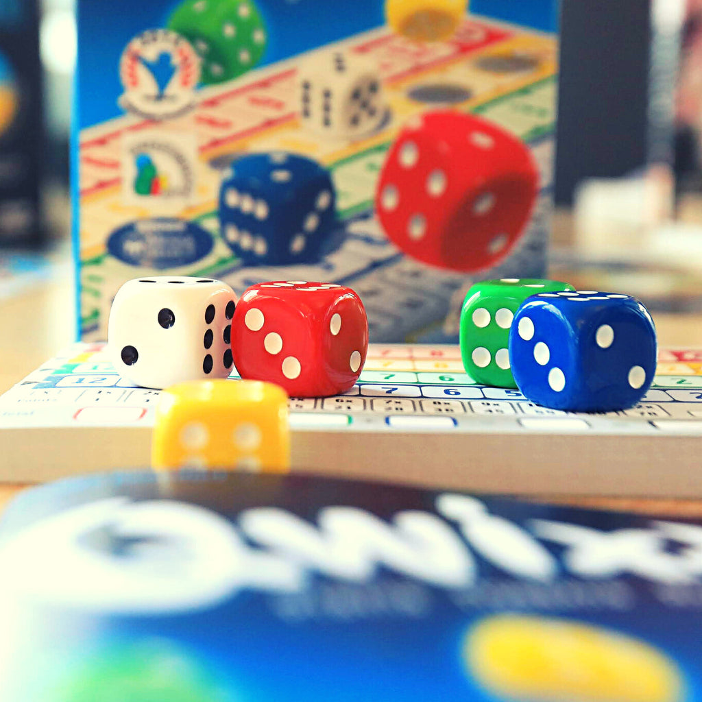 red, white, green, yellow, blue qwixx dice, and a block of score sheets, close up